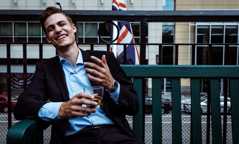 man smiling while sitting and holding whisky glass near concrete building